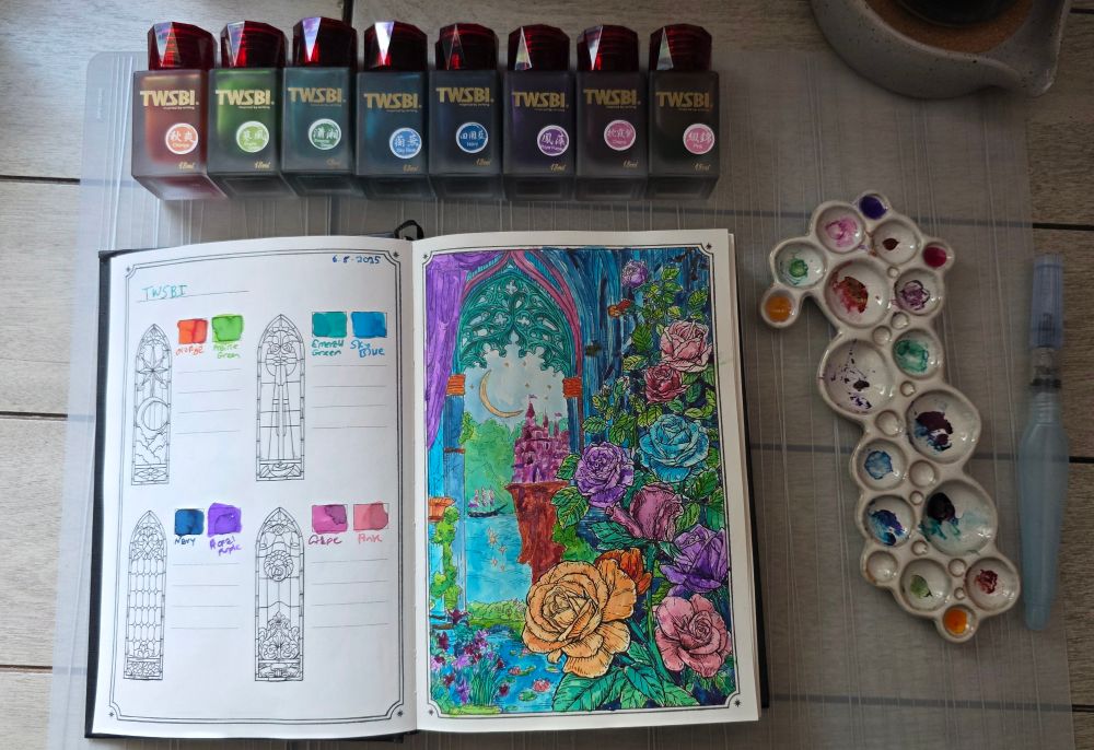 Eight 18ml frosted glass bottles with TWSBI fountain pen inks Orange, Prairie Green, Emerald Green, Sky Blue, Navy, Royal Purple, Grape, and Pink. Dominant Industry Ink Archiving Book, Log of Elixir, open to page with design of roses climbing up a wall and a window looking out to a castle on a cliff, a ship, and the sky filled with a crescent moon and stars, all painted with those 8 inks, and a ceramic paint palette that looks like bubbles with colorful inks in the wells.