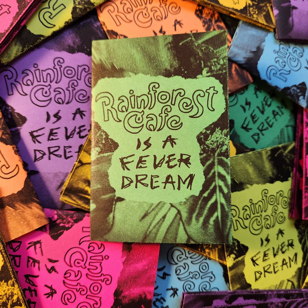 A stack of rainbow colored zines titled "Rainforest Cafe is a Fever Dream."