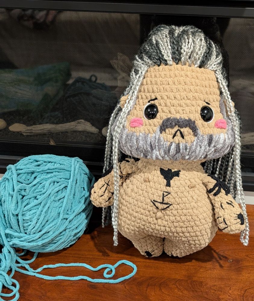 A crochet doll with black embroidered and crocheted tattoos sewn on him 