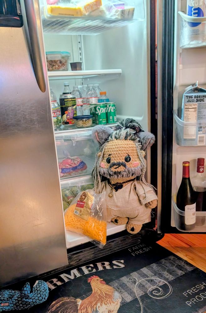 Crochet Ed Teach with a big bag of shredded cheese. He is sitting in an open fridge 
