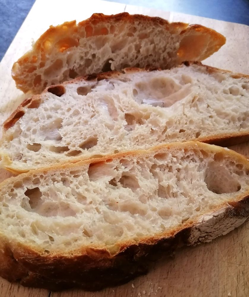 Slices of white sourdough loaf with an airy texture on a chopping board. 