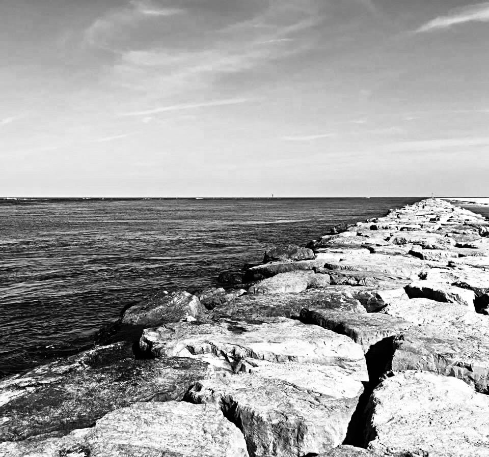 black and white photo of a rock jetty at the ocean 