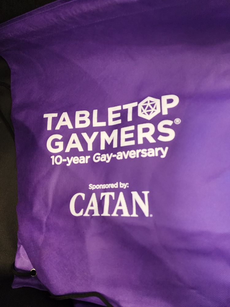 Purple cloth bag with Tabletop Gaymers logo and "10-year Gay-averary". Underneath is Sponsored by CATAN.