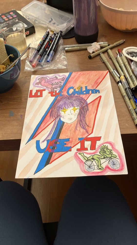 Foto de desenho sobre mesa com materiais soltos. O desenho tem o rosto do david bowie no meio com o corte de cabelo em O labirinto, pintado de roxo. Os olhos são brilhos amarelos. Atrás dele há o clássico raio vermelho e azul.
A frase “let the children use it”  foi separada em duas linhas, uma acima e outra abaixo da cabeça do cantor. Em dois cantos diagonais, artes de blotter: um pégaso e o cara do bycicle 100 anos