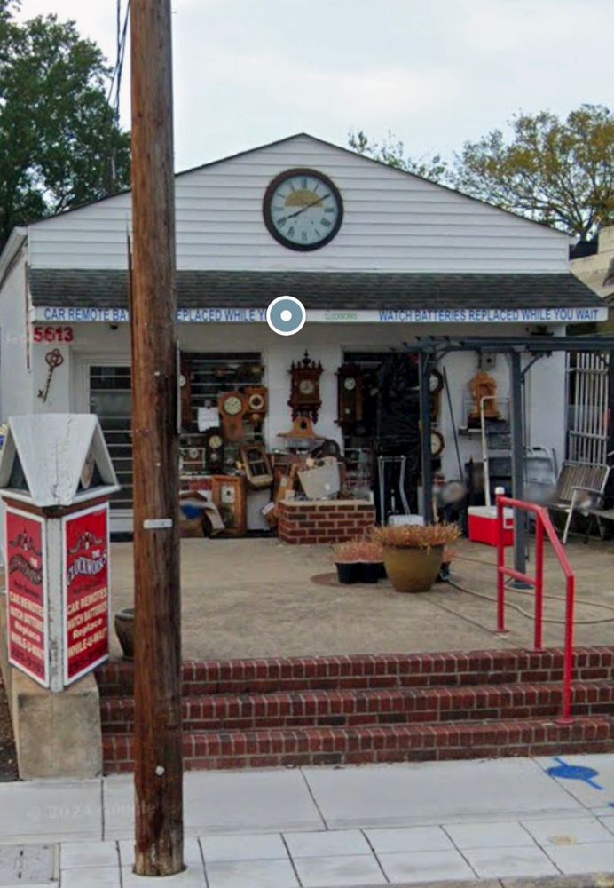 Storefront of Clockworks, a little chaotic with dozens of clocks, mechanical bits, and random things outside. A white building with a red hand rail.