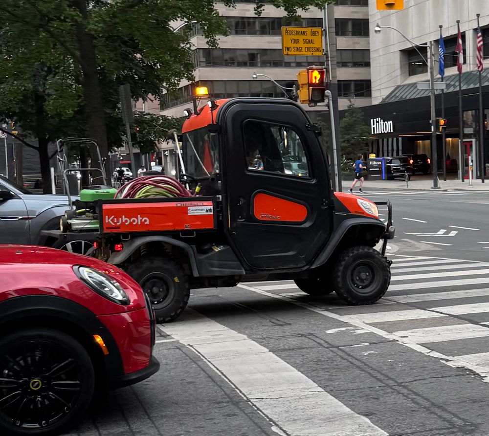 Tiny kubota pickup truck with a lawn mower in the back on University Ave at Richmond St in Toronto. 