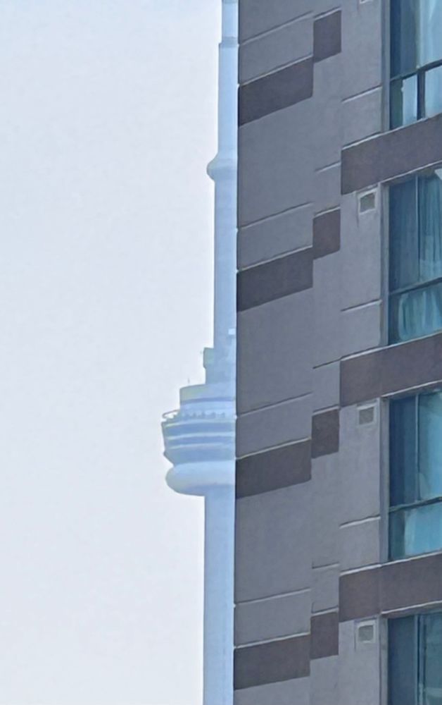 Half of the CN Tower, with the left side visible and the right side blocked by a beige and brown building. 