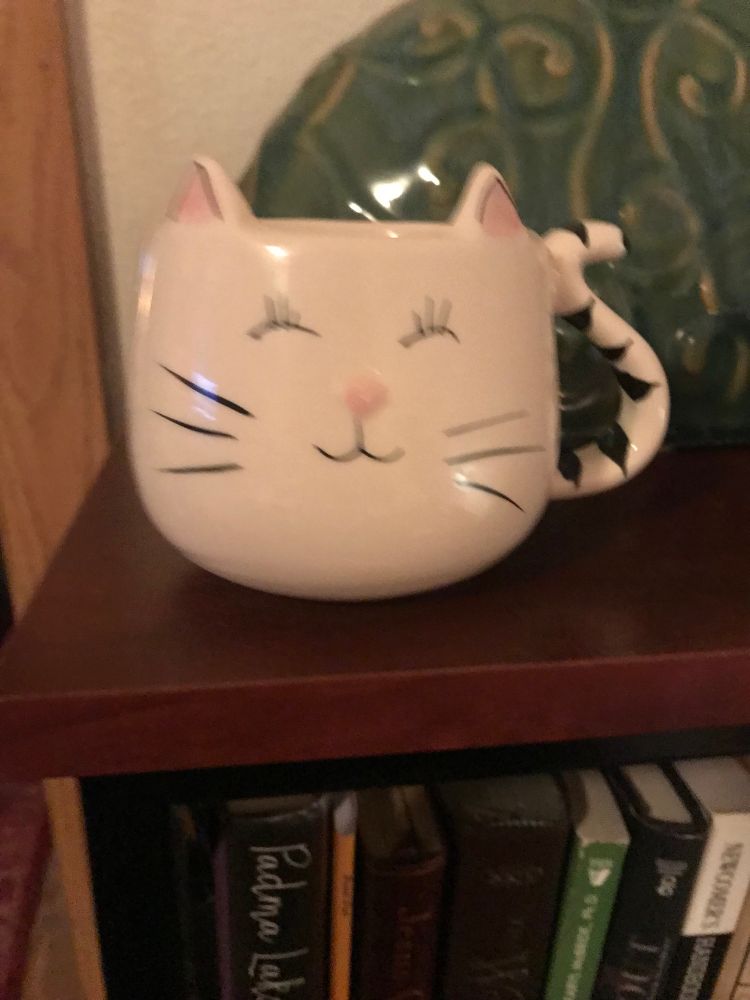 A cream colored mug with a cat’s face painted on it.