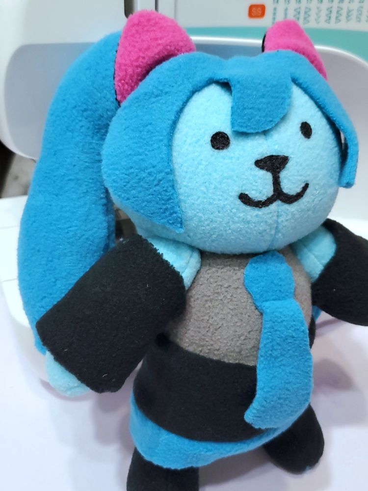 A photograph of a plushie made to resemble a cat version of Hatsune Miku.