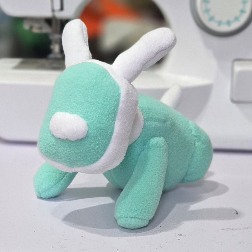 A photograph of a plush toy made to resemble an iDog music speaker from the early 2000s. It is a seafoam green color with white trim.