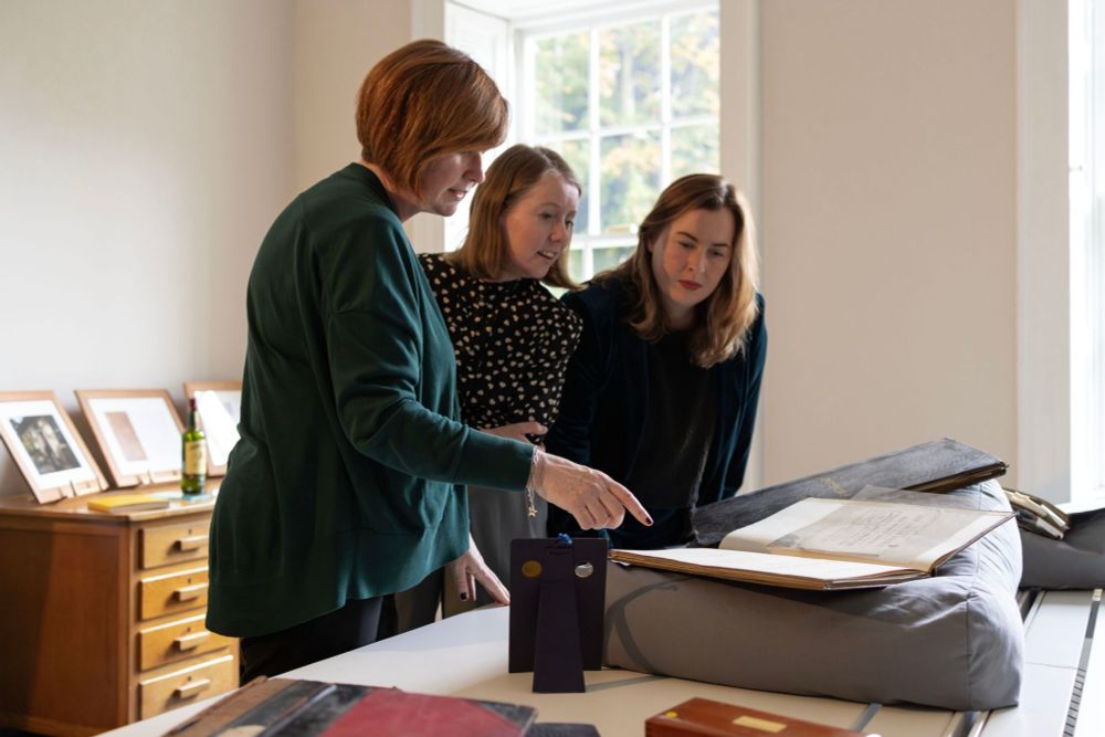 Three women gathered around a table, intently examining a book placed in front of them.
