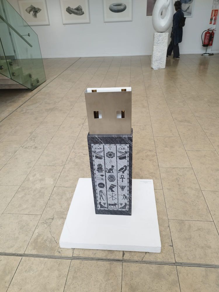 A sculpture in metal and stone shaped like a USB key, decorated with Egyptian hieroglyphics.