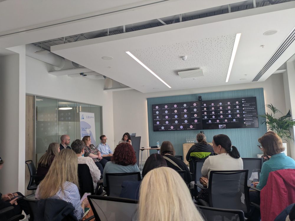 A diverse group of people seated in a well-lit room, engaged in conversation and sharing ideas.