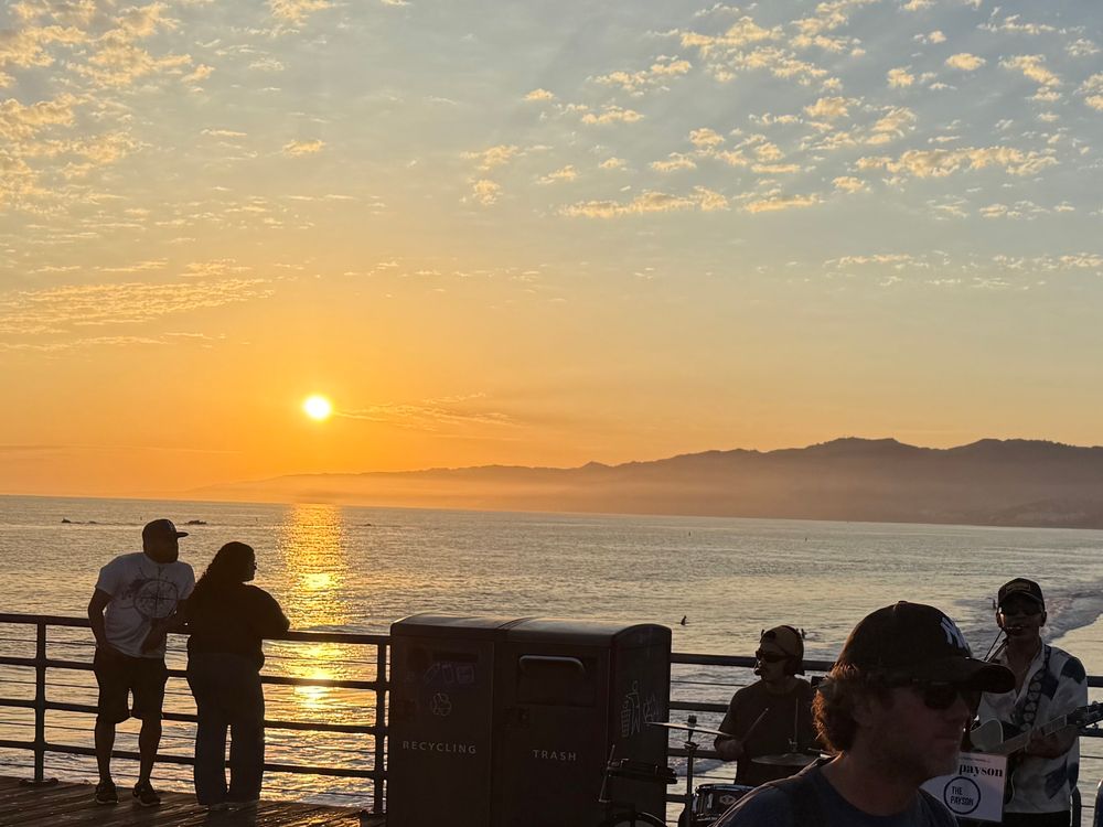 Photo of the Pacific Ocean from Santa Monica Pier, facing northwest toward the setting sun. The sun is still well above the horizon.