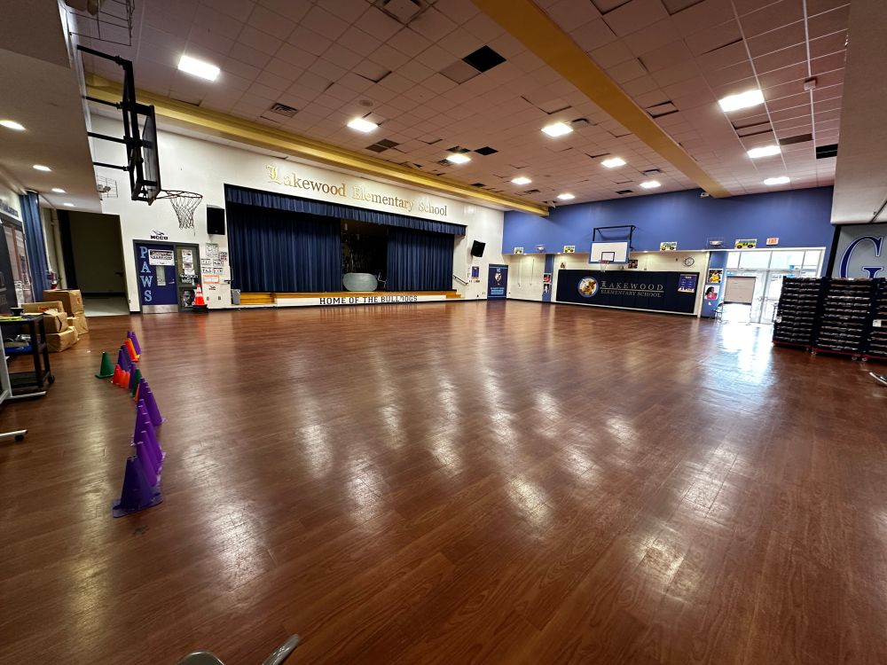 Photo of the Lakewood Elementary School gym, empty except for racks of bread barely visible on the right-hand side 
