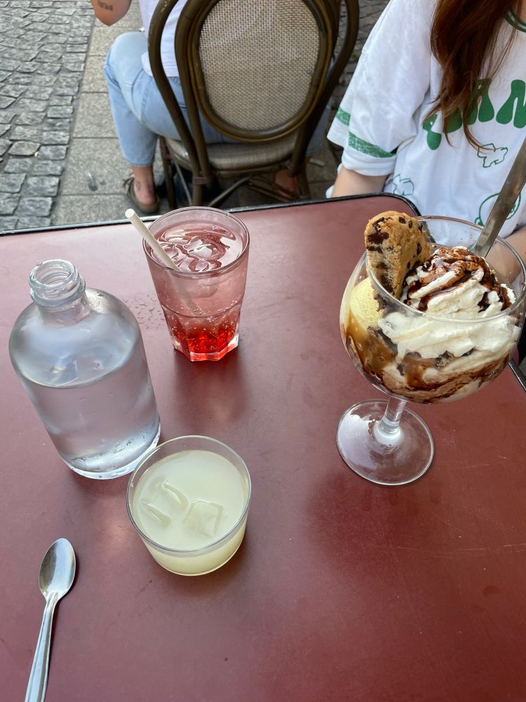 Table en terrasse avec Romane et Zoe. Il y a un pastis, un diabolo grenadine et une coupe glacée aux cookies sur la table.