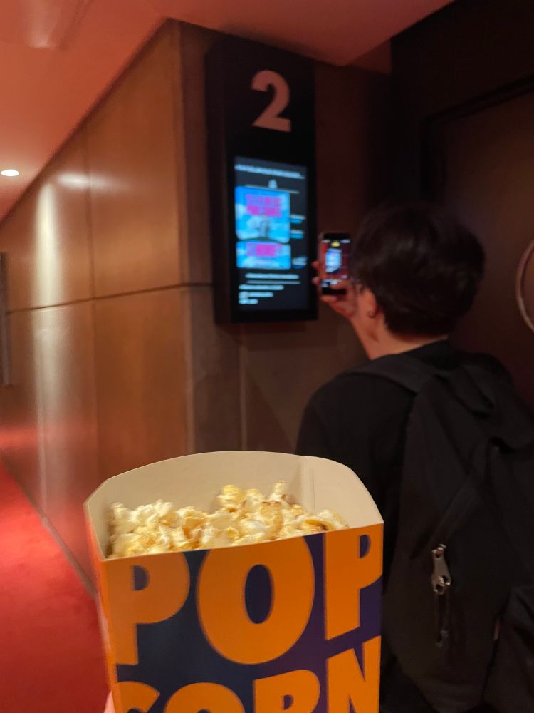 Pop corn au premier plan et Lena qui prend en photo le panneau de la salle 2 du cinéma avec le film Y a-t-il un flic pour sauver le monde ? (The Naked Gun).