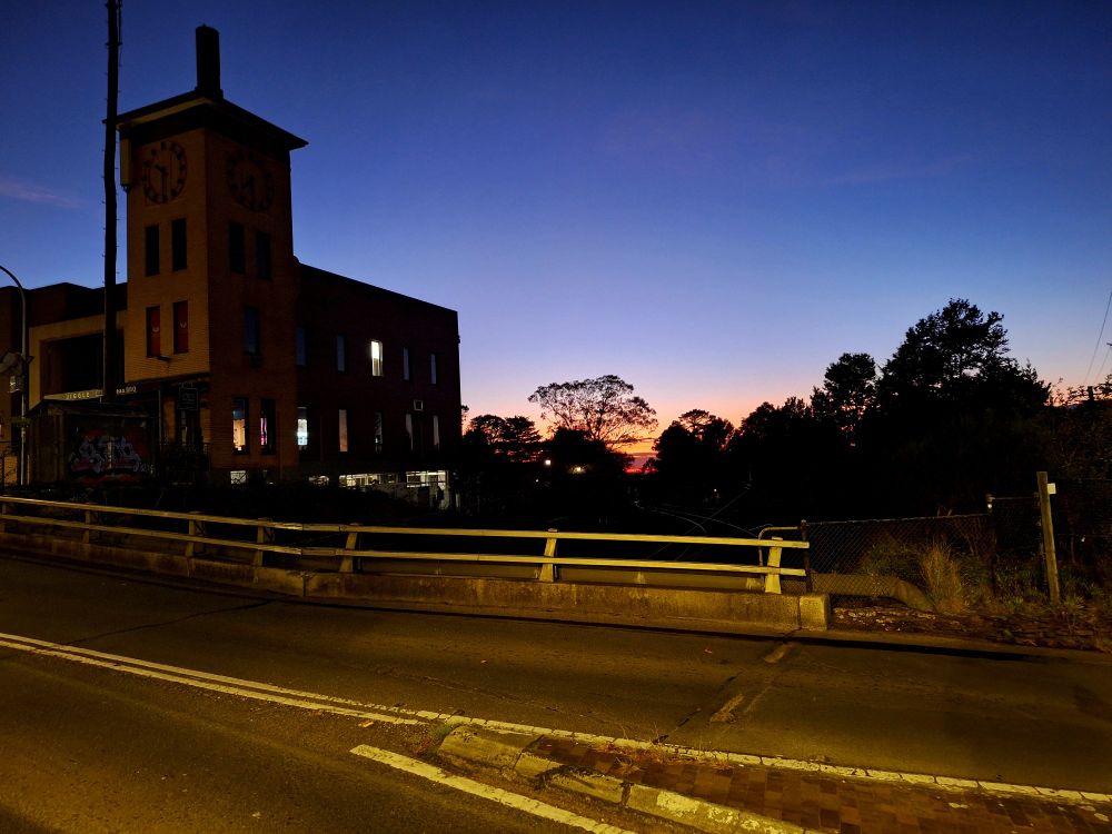 View of a pink sunrise, with a slightly dilapidated road in foreground and an ugly brick building beyond. 