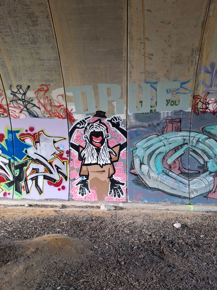 Several bits of art spray painted on a tunnel wall. The central panel is a black figure with 4 hands.