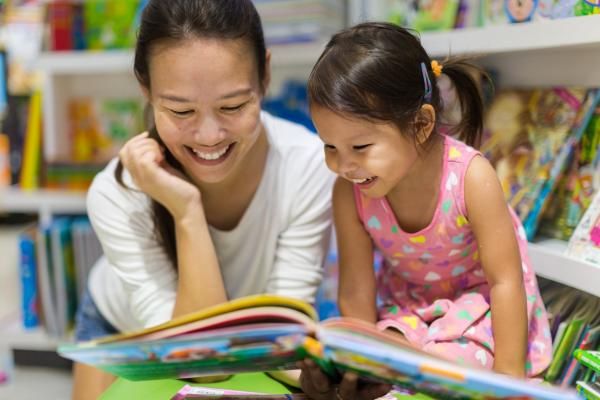 An asian mother and daughter read a picture book together in a children's library.