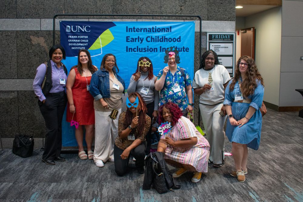A group of attendees pose in front of an Inclusion Institute sign. They hold various photo booth props.