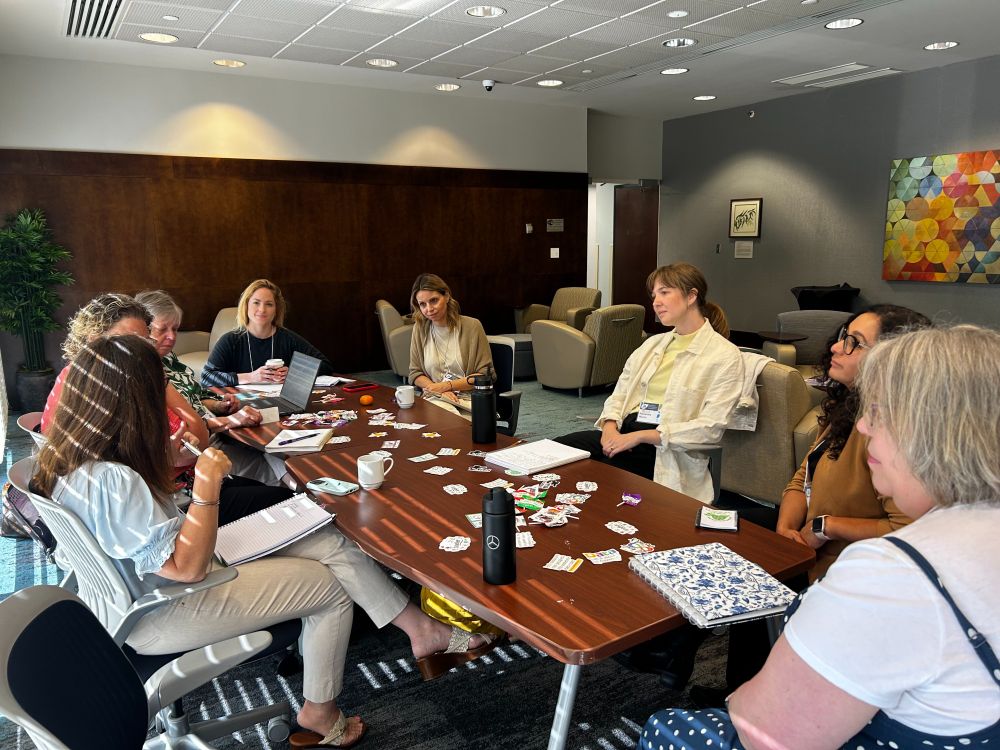 A group of eight people sit around a table in discussion.