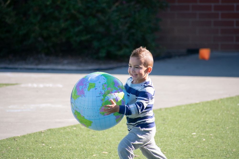 A young boy runs in a schoolyard while holding an inflatable globe.