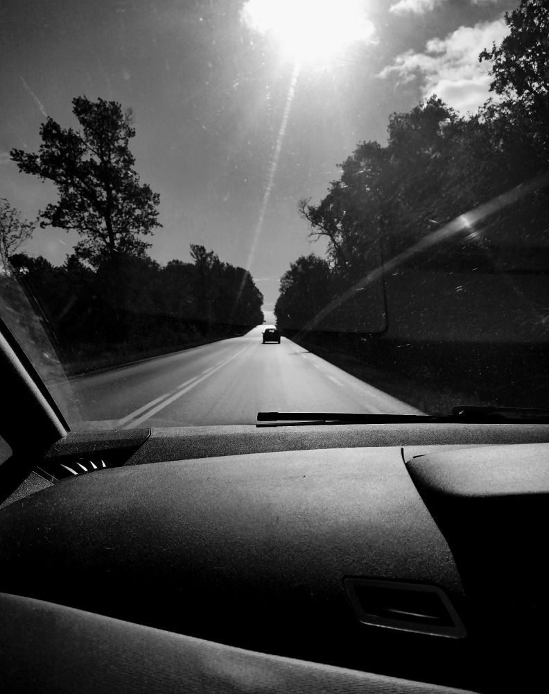 black and white shot through car windscreen of single car on empty road