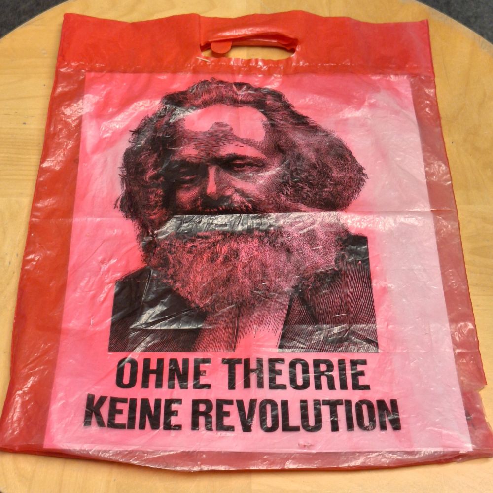 Rote Plastiktüte (Vorderseite), darauf in Schwarz gedruckt ein Bild von Karl Marx und der Slogan »Ohne Theorie keine Revolution«.