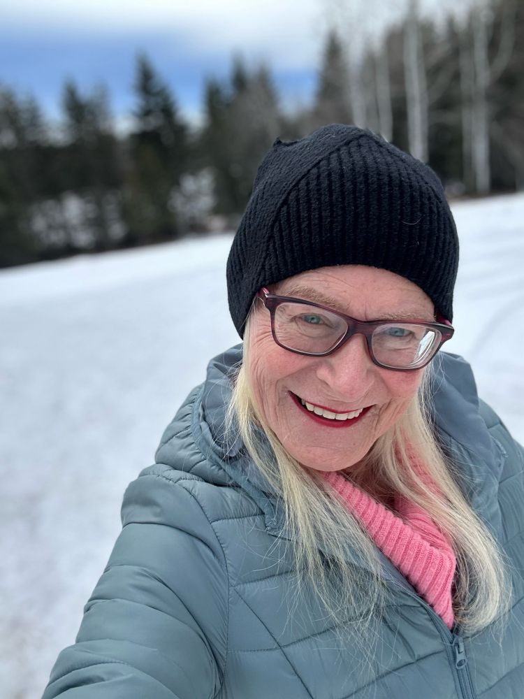Trans femme senior takes a wintry selfie wearing a splash of pink and a smile.