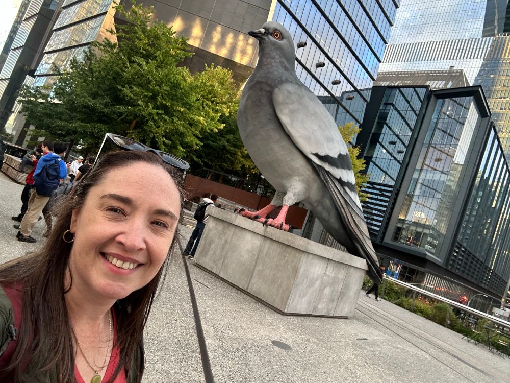 A tired teacher, who had parent teacher conferences the night before, smiles in front of a giant statue of a pigeon on NYC’s High Line Park. 