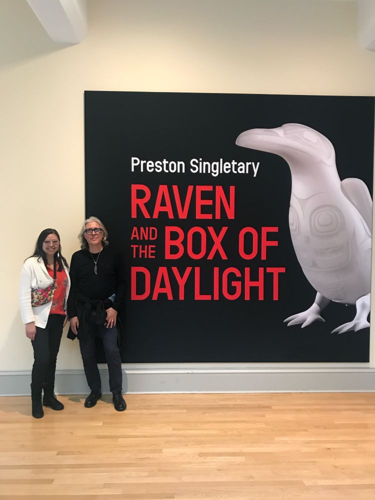 Miranda and Preston standing next to exhibit poster that says “Preston Singletary: Raven and the Box of Daylight”