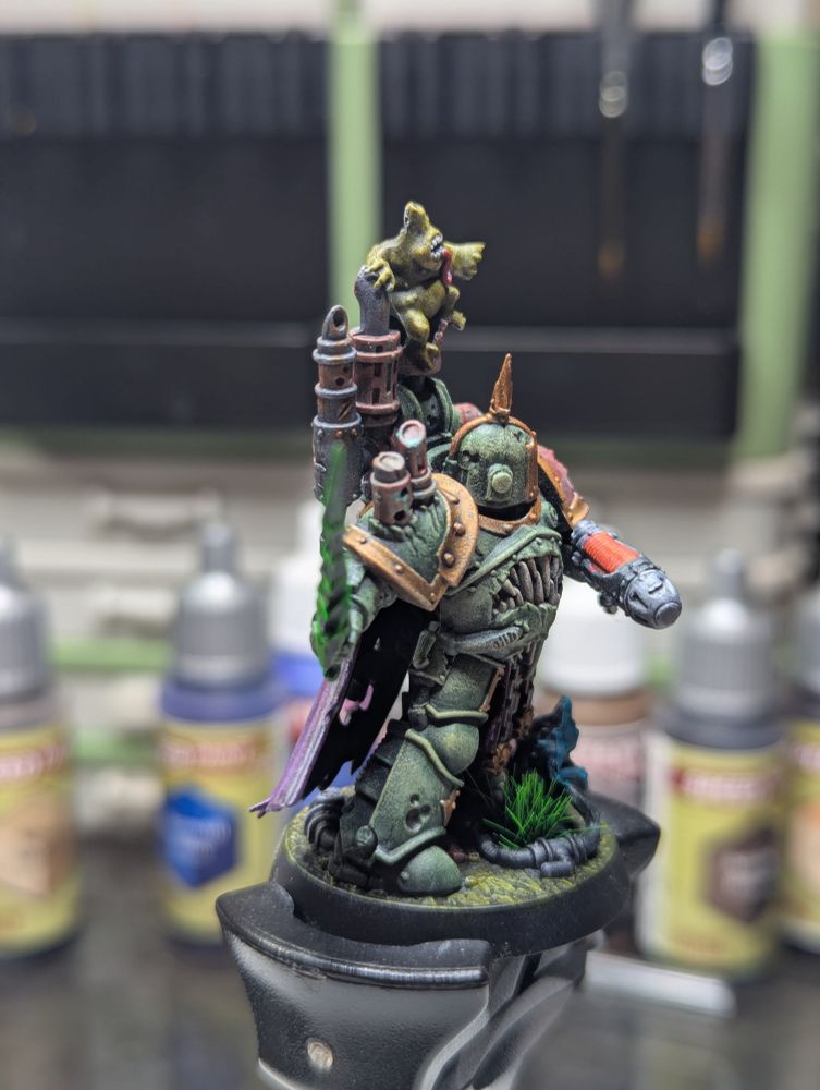 A Death Guard Champion wielding a sword and plasma pistol, clad in green power armor and joined in battle by 2 nurglings