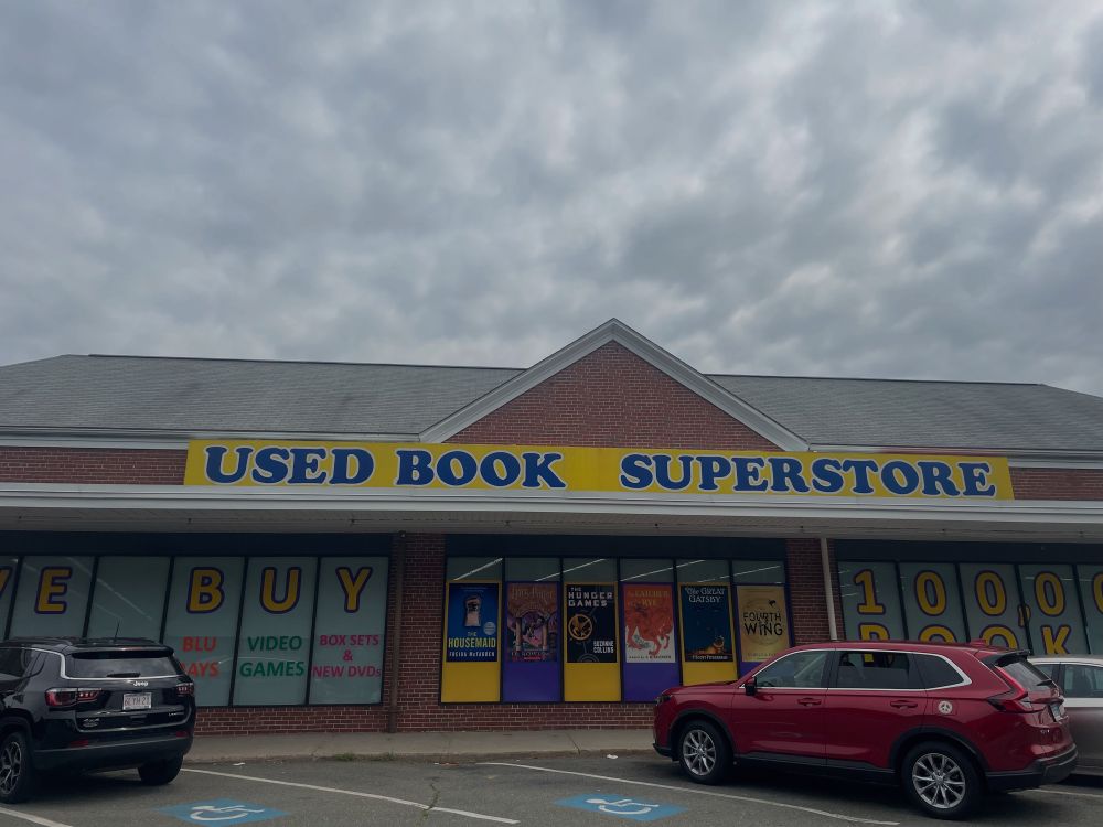 View of a VERY LARGE storefront with the name “Used Book Superstore” in blue text on a yellow background.