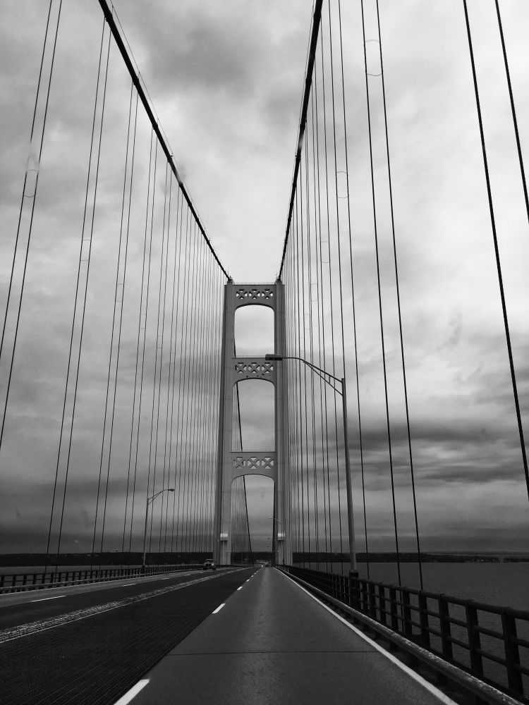 Monochrome image of a road leading across a tall bridge. Ominous clouds overhead.