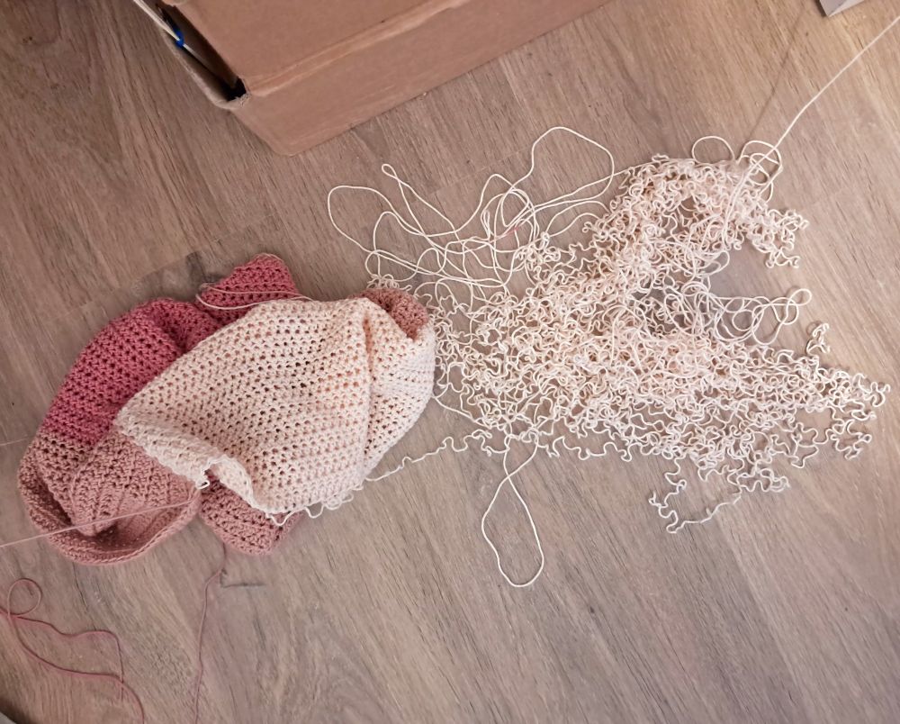 Un projet de t-shirt au crochet dont partent des fils. Un tas de fil â côté permet de comprendre que le projet est en train d’être défait.