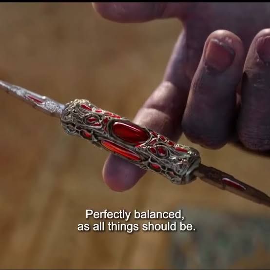 Imagem do filme "Vingadores - Ultimato", onde o personagem Thanos segura uma pequena adaga no meio com o dedo indicador, e há a fala legendada (em inglês, aqui traduzida) "perfeitamente equilibrada, como todas as coisas devem ser".