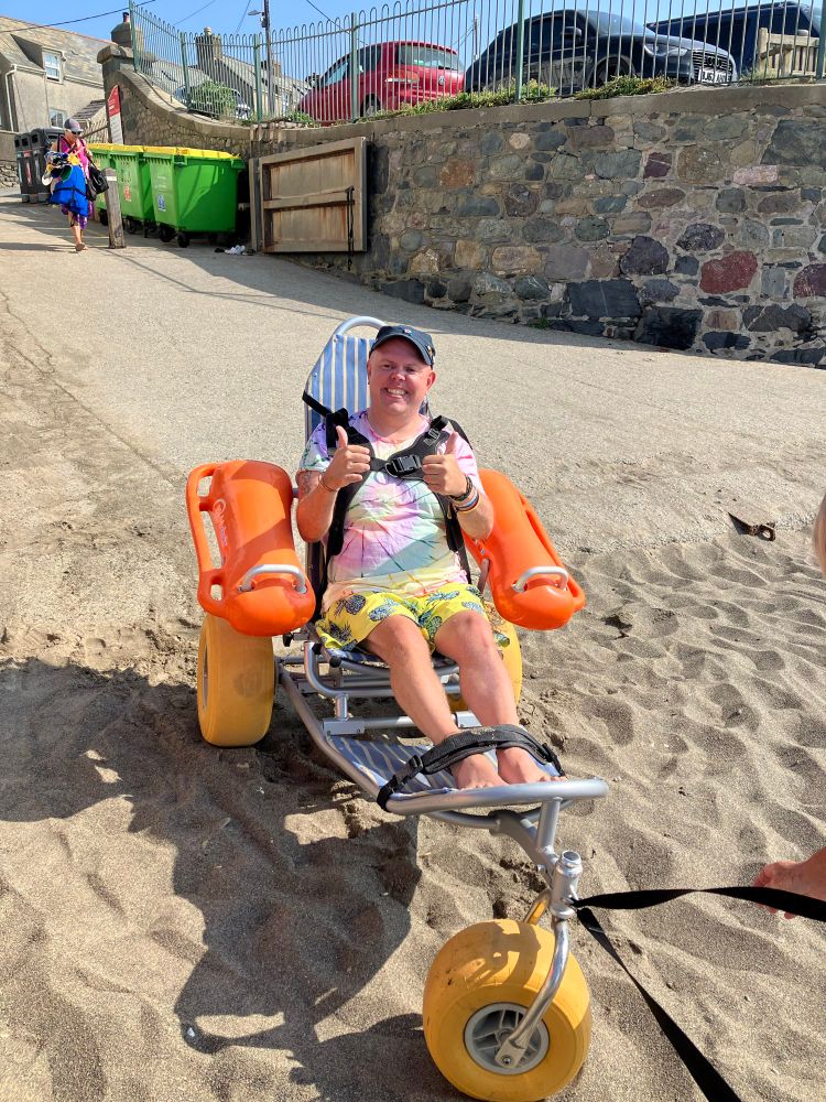 I’m sat in a bright orange beach wheelchair on the sand, grinning in my tie-dye shirt and yellow shorts, giving two thumbs up.