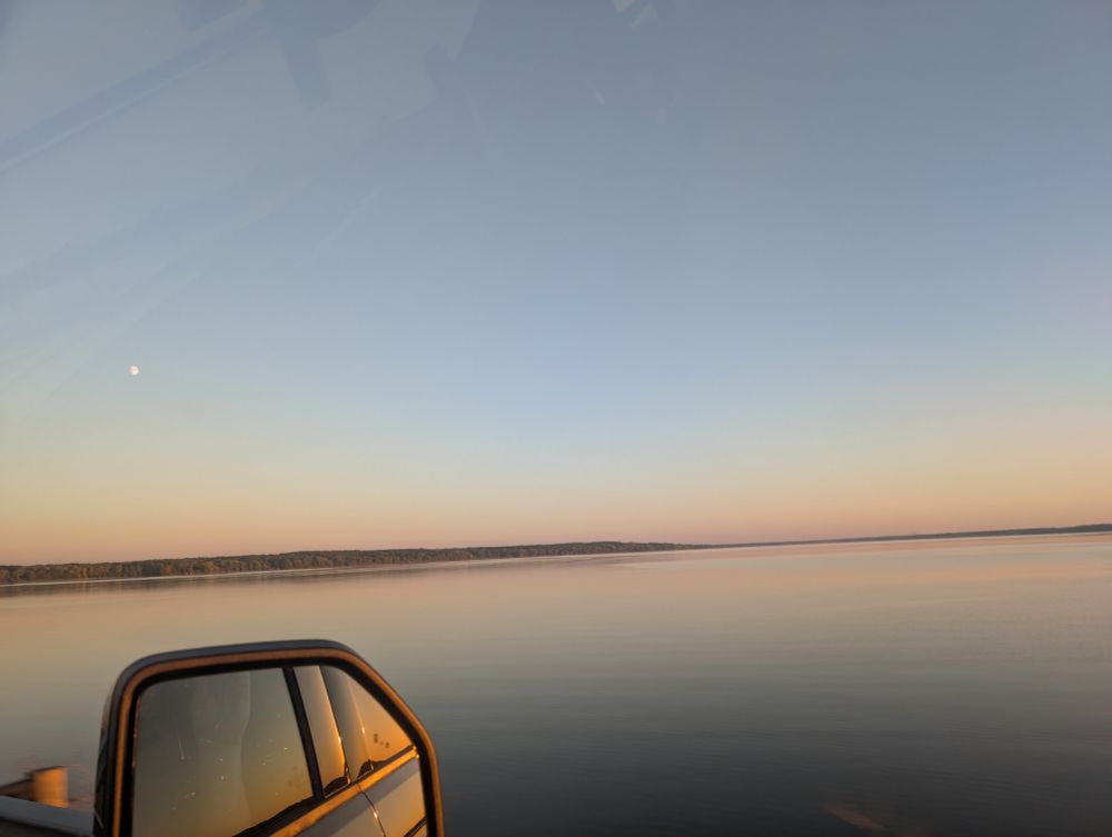 Looking out a truck window across Lake Pymatuning. The sky is pastel shades, and the moon is visible to the upper left