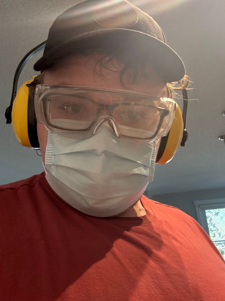Me wearing yellow earmuffs as hearing protection, a black baseball cap, safety glasses and a blue mask