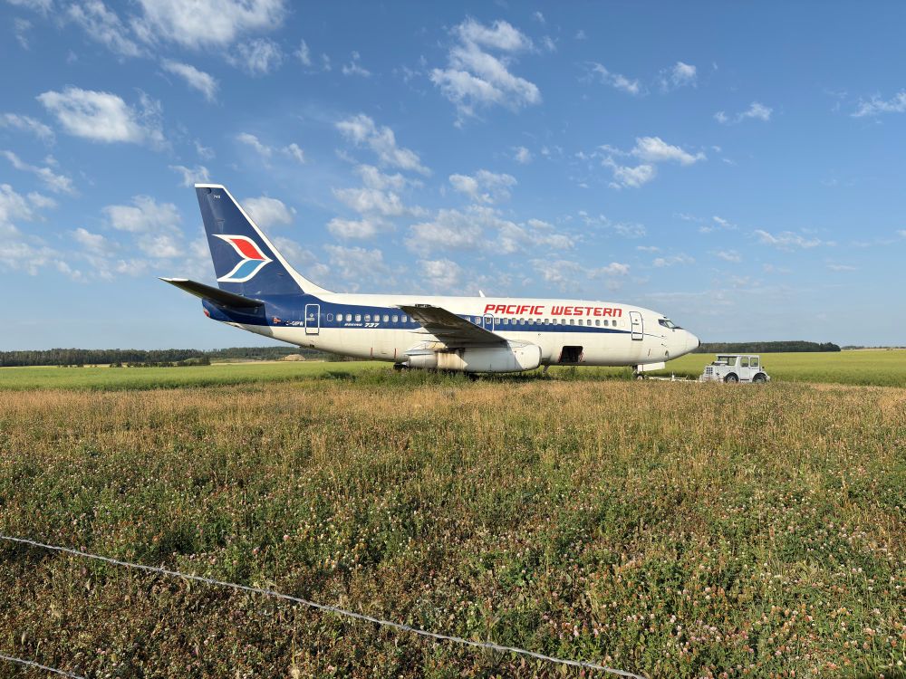 A Boeing 737-200 airplane sitting in a field with a tug vehicle attached. Registered C-GIPW, it used to fly for Pacific Western Airlines and still retains its livery.