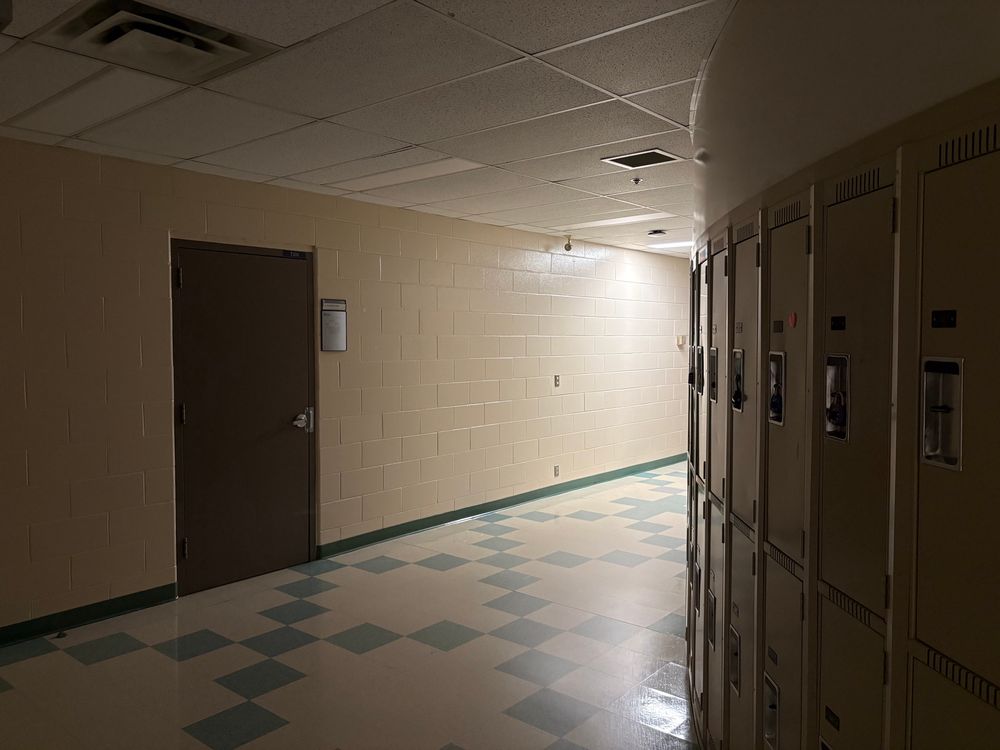 A school hallway corridor; the lights are off except for ones just around the corner, making an unsettling effect