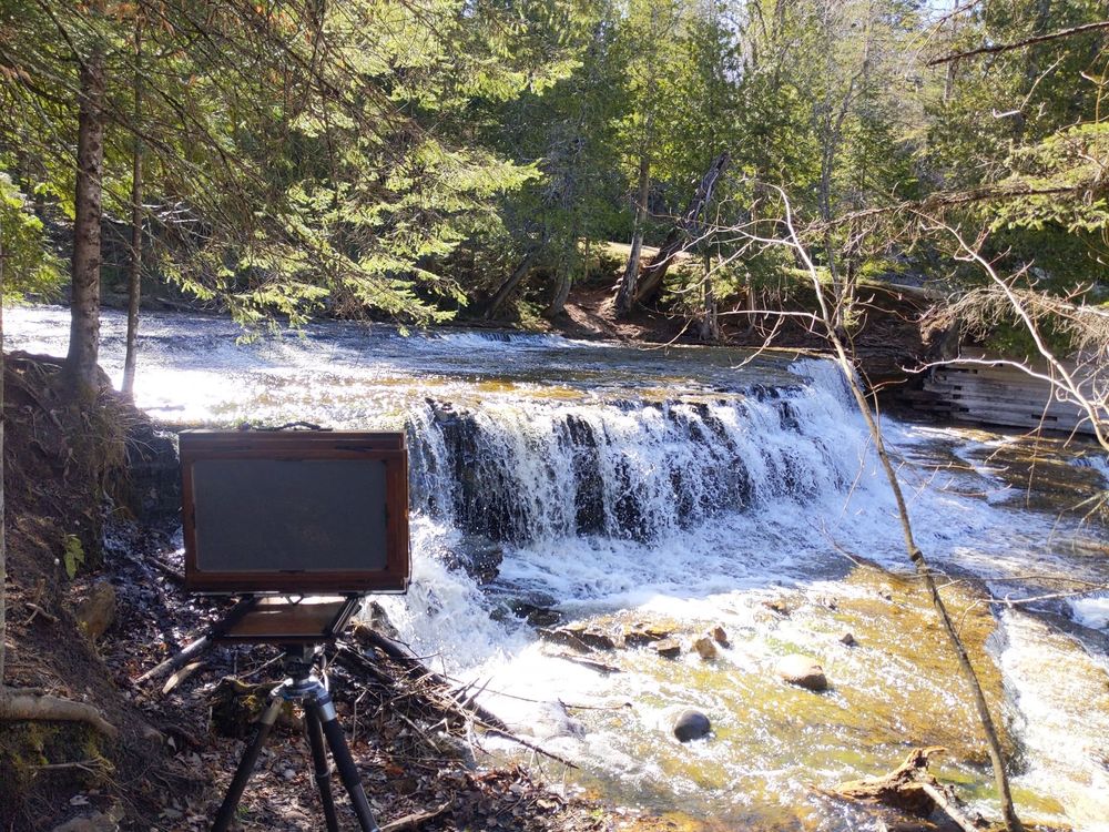 A massive 12x20" banquet panoramic camera sits atop on tripod, capturing a large, flowing waterfall that is backlit by the afternoon sun. 