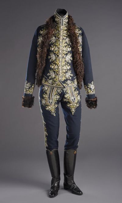 FRONT VIEW source: "The dress is made of dark blue felt. The attenuated mente with set-in sleeves reaches below the waistline the borders are embroidered with alternating motifs of big and small bunches of flowers, in green and white silk thread. Lined with brown lamb's fur, a later addition. The cut of the waistcoat's shoulders are curved it is attenuated at the back and reaches below the waistline. Its width is adjustable with a lace at the back. The borders and the standing collar are embroidered with the motifs described above. Decorated with white and green silk braids all around. The waistcoat (Inv.nr. 14857.) can be closed with braided buttons and loops knit of silk thread its front lower part has a slanted cut.

This dress represents some special features of the 17th century Hungarian man's fashion: the slanted cut at the front and the braided buttons and loops. On the other hand, these features appear on a waistcoat that, following the fashion of Western Europe, took the place of the typical Hungarian "dolman" in the 18th century. The European influence is apparent on the attenuated cut, as well as on the set-in sleeves and the curved line of the shoulders. The legs of the trousers (Inv.nr. 14856.) are tight-fitting for boots, and are with a flap. The bottom consists of two pieces the cut is identical with the usual type of cut of the 17th century. The side seams are braided and embroidered with motifs similar to those of the waistcoat and the mente."