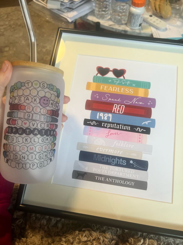 a picture of christmas presents from my sister in law. on the left is a tumbler with each taylor swift album listed as a friendship bracelet. on the right is a framed photo of each taylor swift album listed as a book.