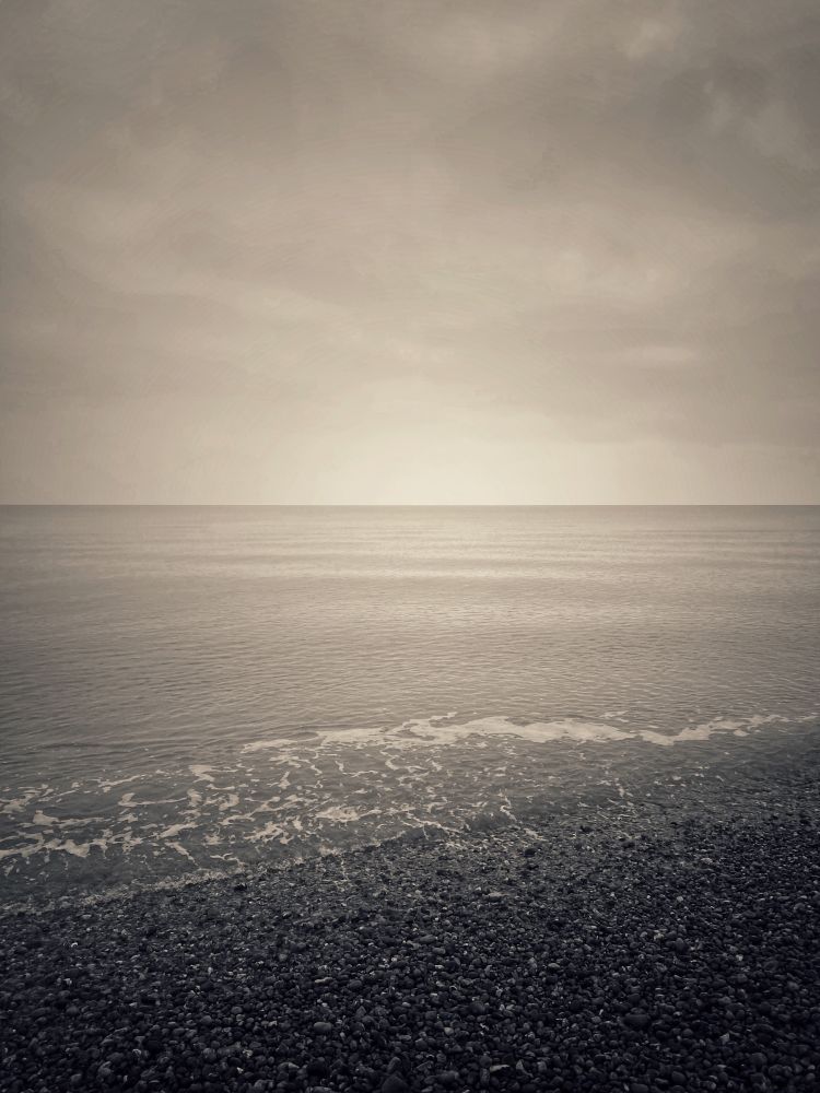 Sepia image of calm sea and shingle beach