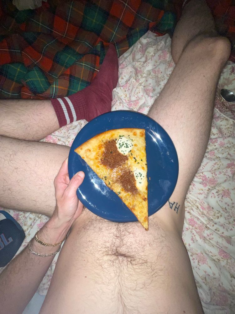 Naked me laying on my bed with a slice of pizza on a plate covers my cock. 