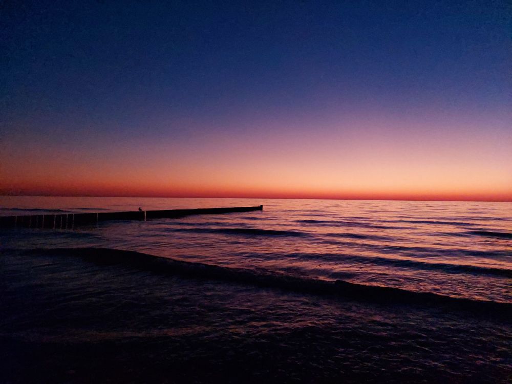 Photo of the ocean. The sky and water are colored in dark blue, purple, orange, and pink