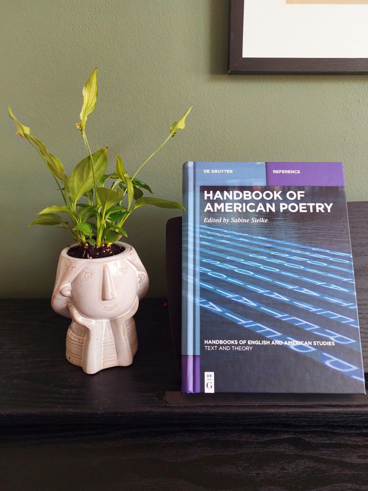 Photo of a book with blue and purple cover propped up on the sheet music stand of a piano. There is a plant next to it in a pot in the shape of a girl's or woman's head and torso. The female figure is smiling contently, while the plant looks like wild ideas sprouting from her head.