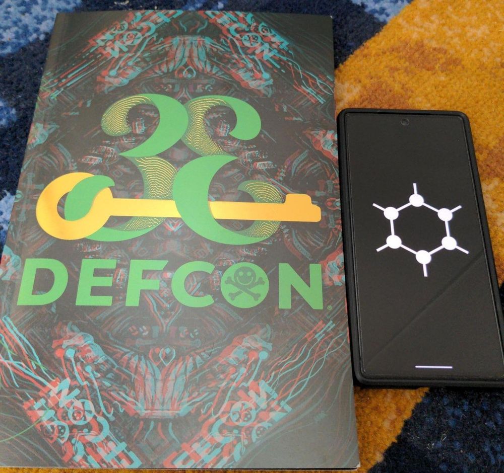 Defcon printout next to phone showing GrapheneOS logo